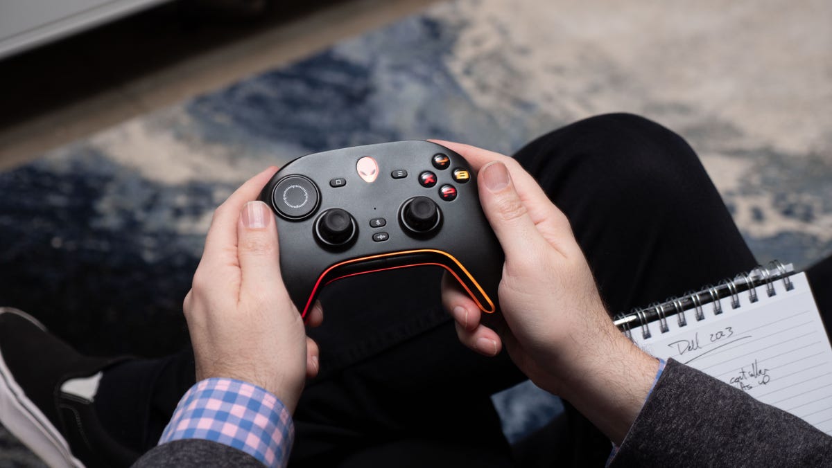 руки держат черный игровой контроллер с логотипом Dell Alienware в качестве центральной кнопки