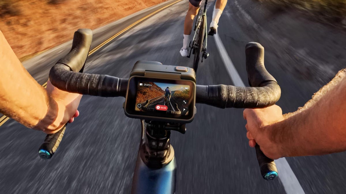 The Insta360 Ace Pro action cam with its rear display tilted up while mounted on the handlebars of a bike and displaying the road ahead being captured by the camera..