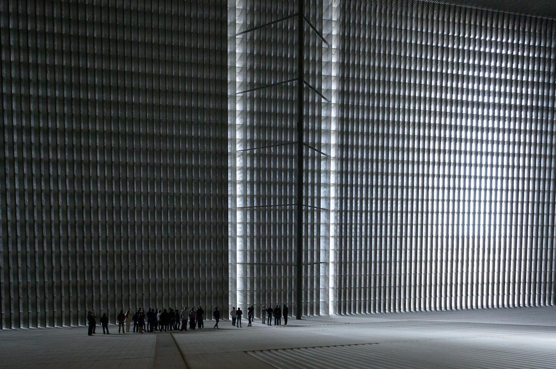 A group of people look tiny inside a wind tunnel facility with tall gray walls.