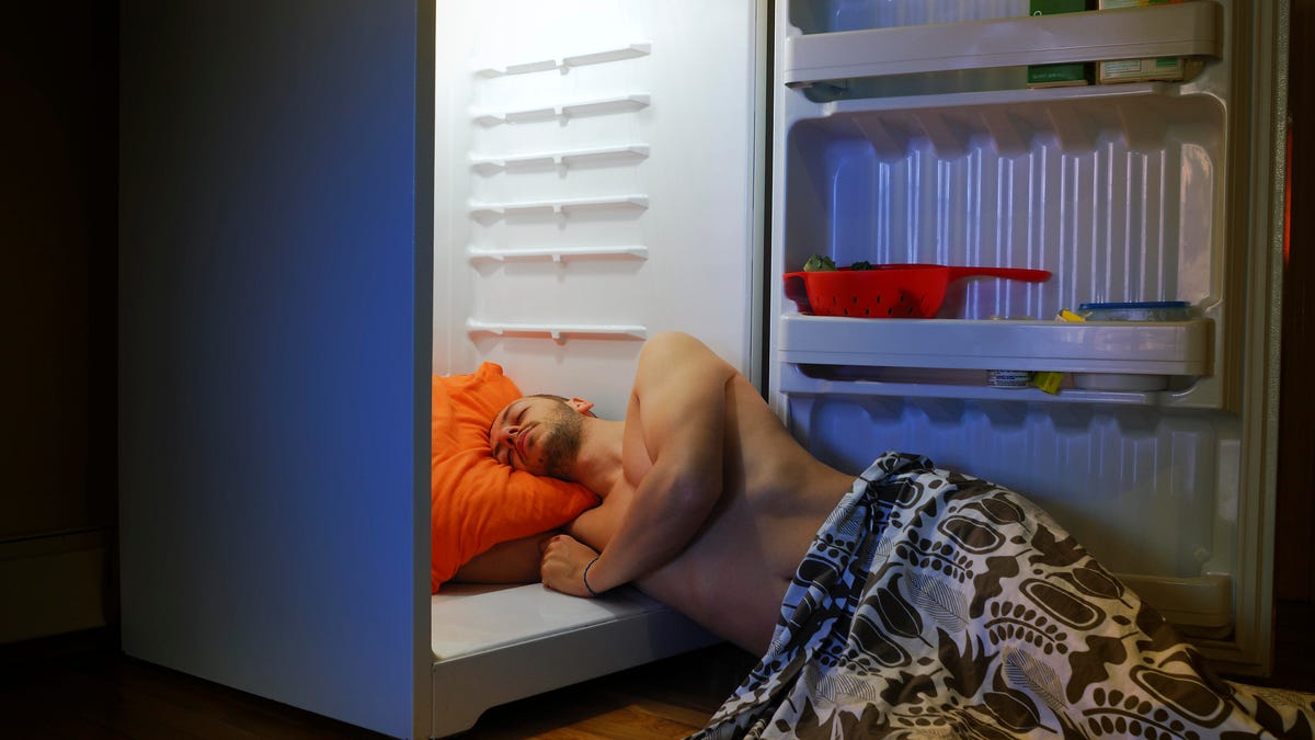 Shirtless man on the floor with his upper body in an open fridge while sleeping. 