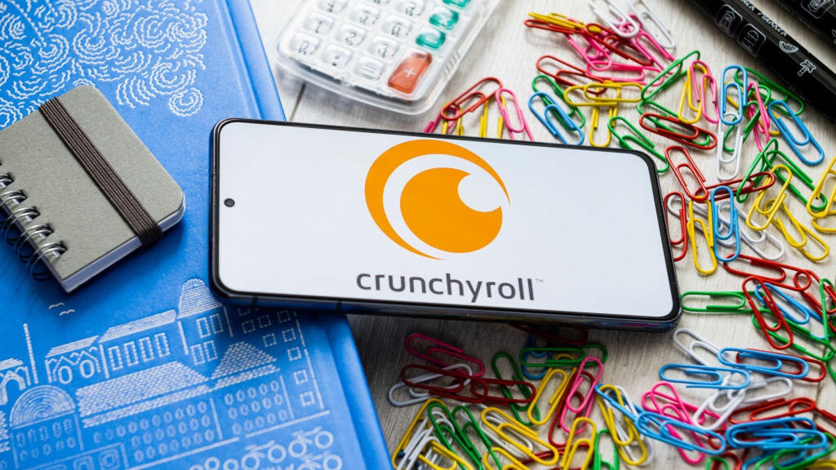 Crunchyroll logo on a smartphone on top of a pile of paperclips and other office supplies
