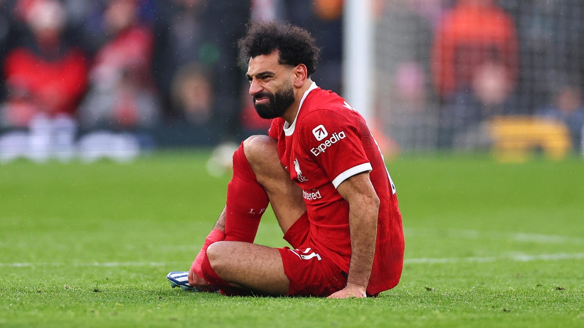 Mohamed Salah of Liverpool wincing and holding his ankle while sitting on the pitch.