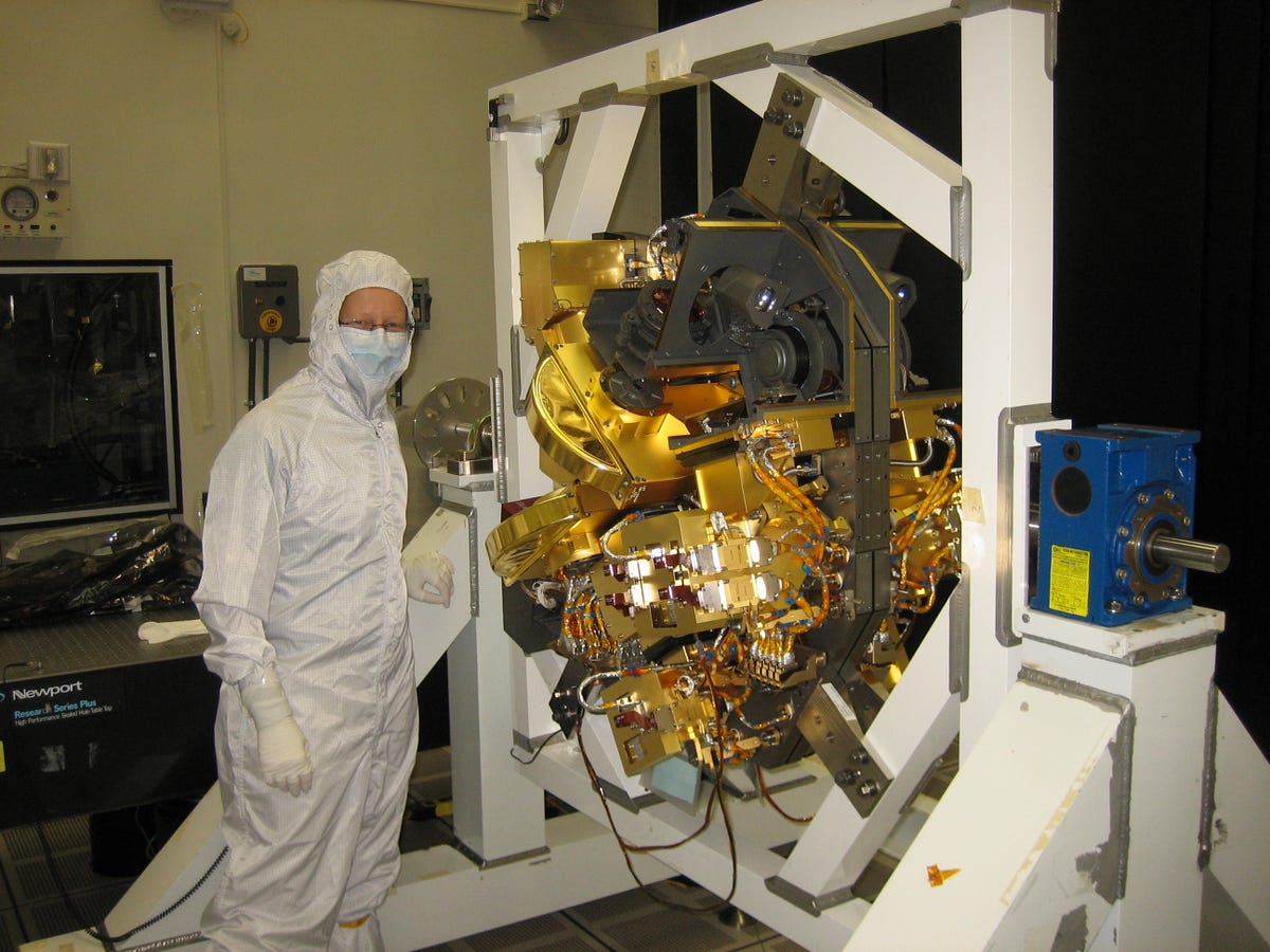 An engineer in a bunny suit stands next to Webb's NIRCam.