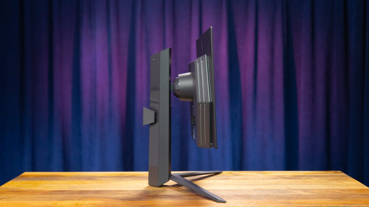 The side of the LG Ultragear OLED 27-inch monitor on a wood surface with a blue and purple curtain in the background