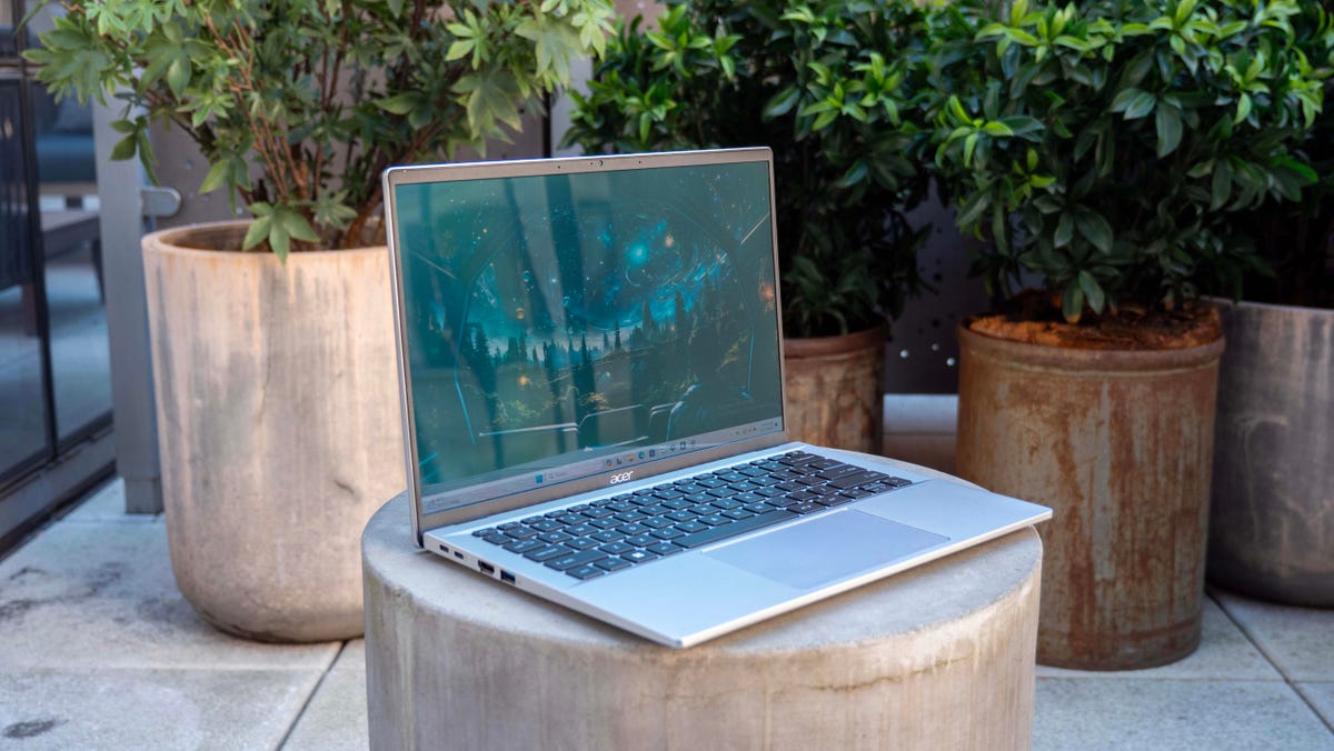Acer Swift Go 14 laptop open face front angled to the right sitting on a concrete stool with plants in the background.