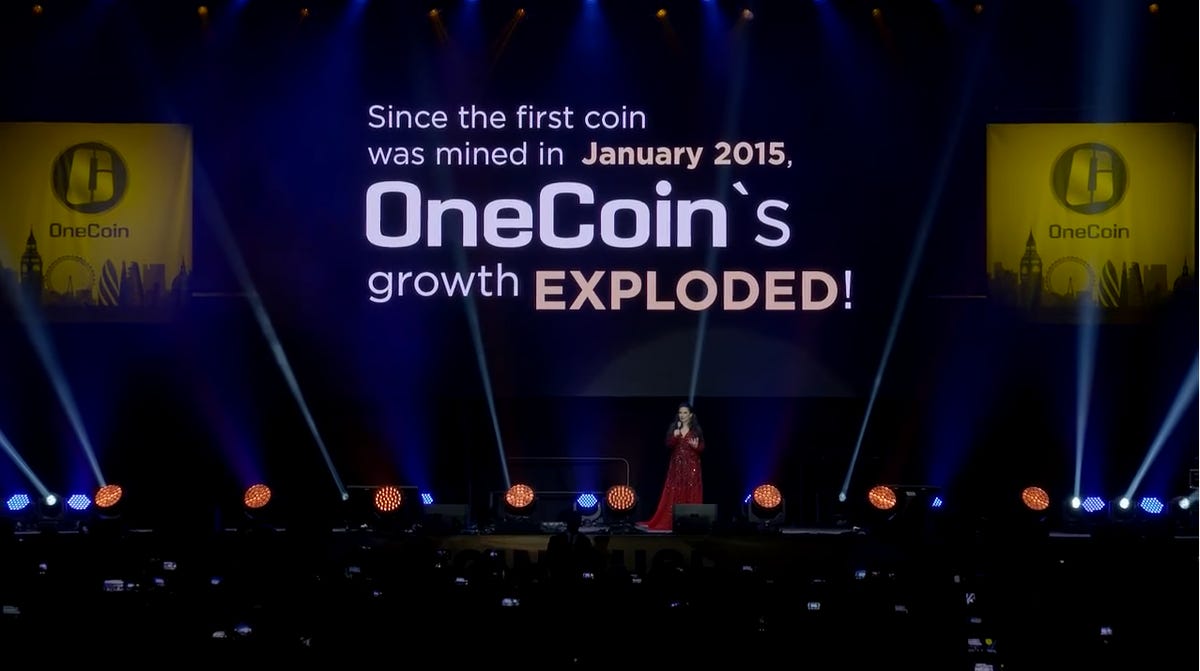 OneCoin founder Ruja Ignatova on stage under a sign that reads 