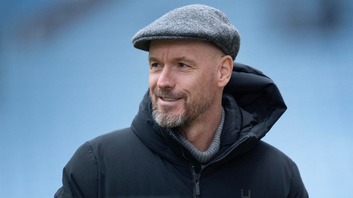 Manchester United manager Erik ten Hag looking to his right hand side, smiling, wearing a cap.