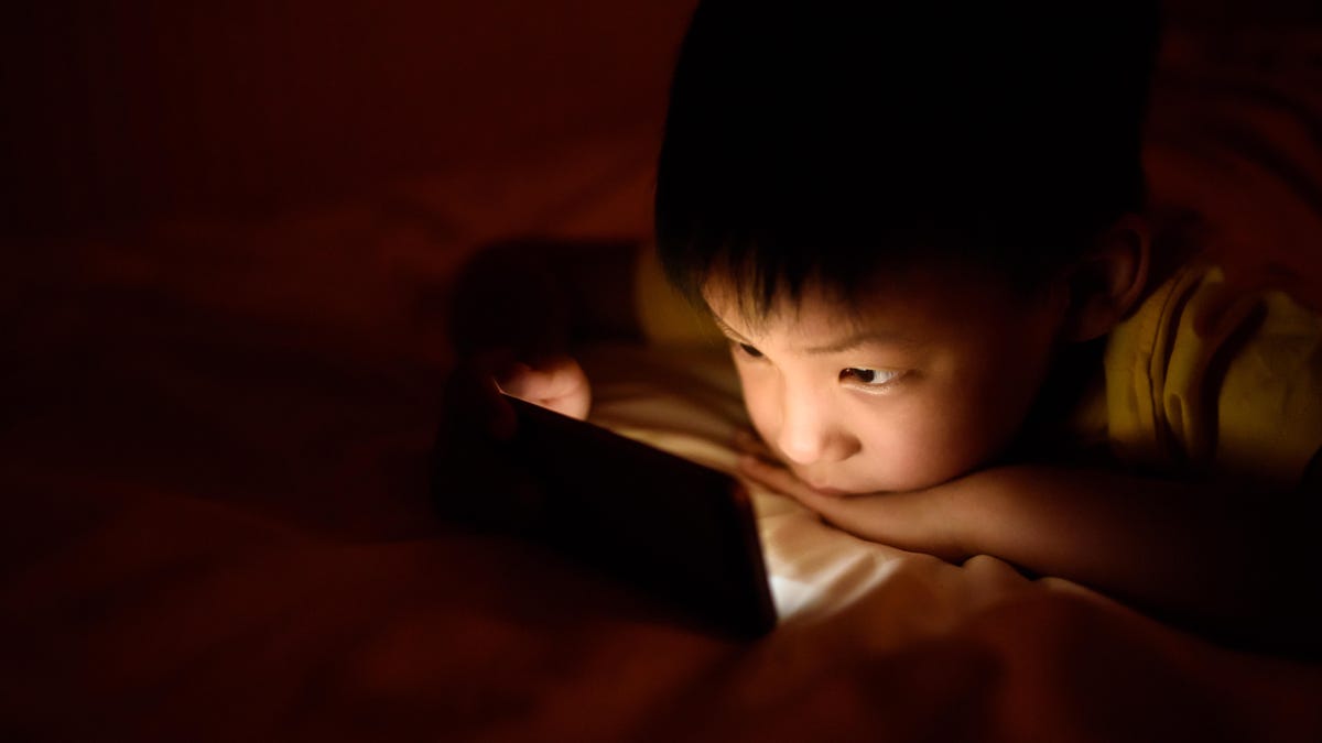 A young boy's face is illuminated by a phone screen