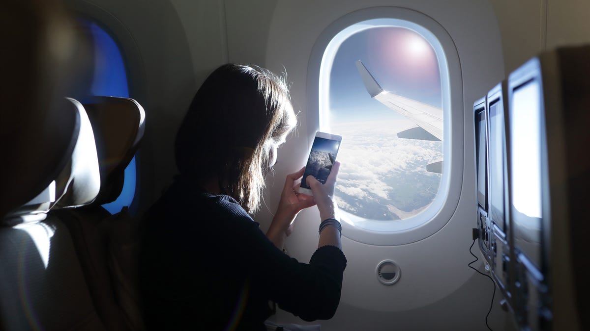 A woman takes a picture out a window, with the airplane's wing and the sun in the distance.