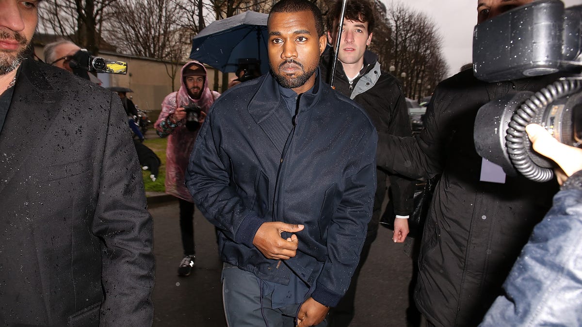Kanye West walking in the rain with his security around him