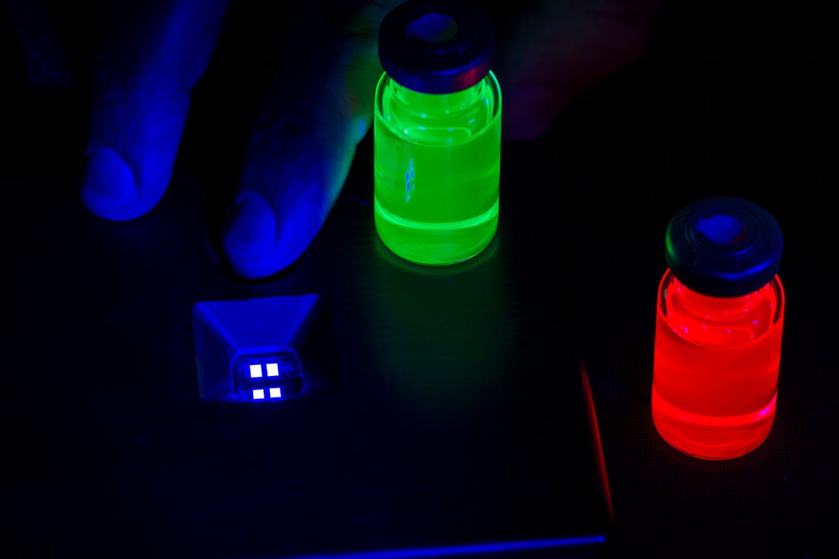 Frascos vermelhos e verdes de pontos quânticos fotoluminescentes ao lado de um protótipo QD eletroluminescente azul.