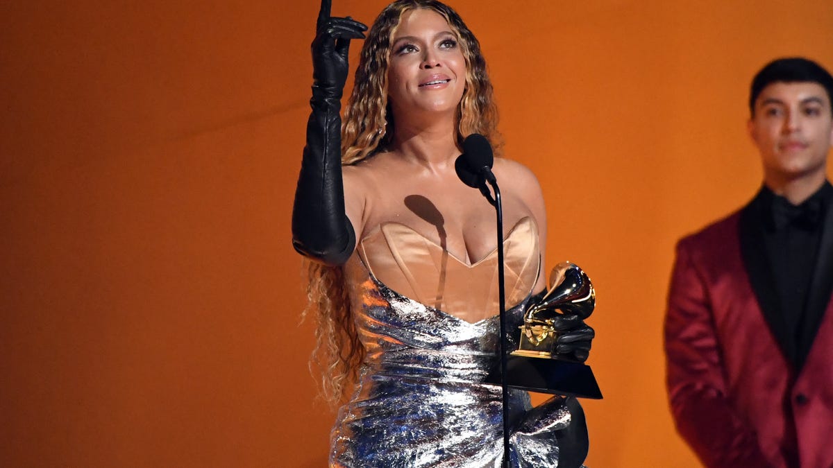 Beyonce standing on stage with her Grammy, pointing and looking up