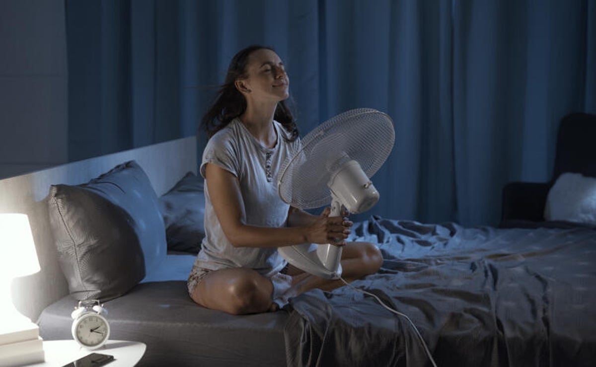 Woman holds a fan near her face before sleeping.