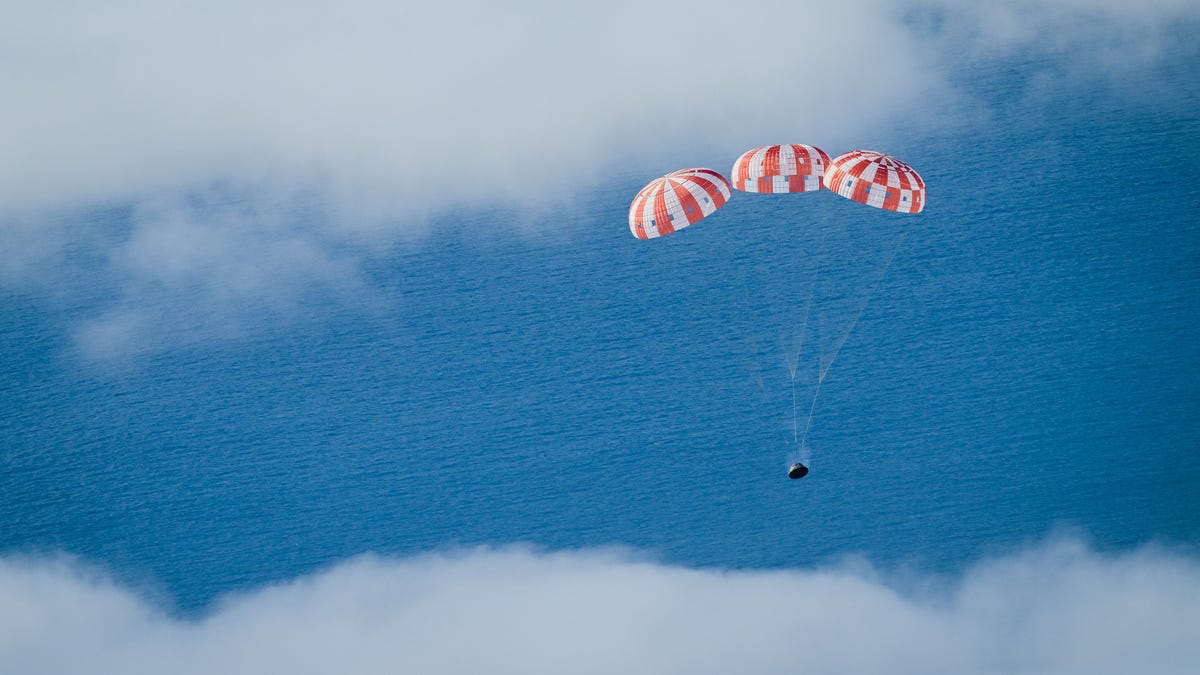 A red and white striped parachute brings Orion down to the Pacific ocean amid the clouds.