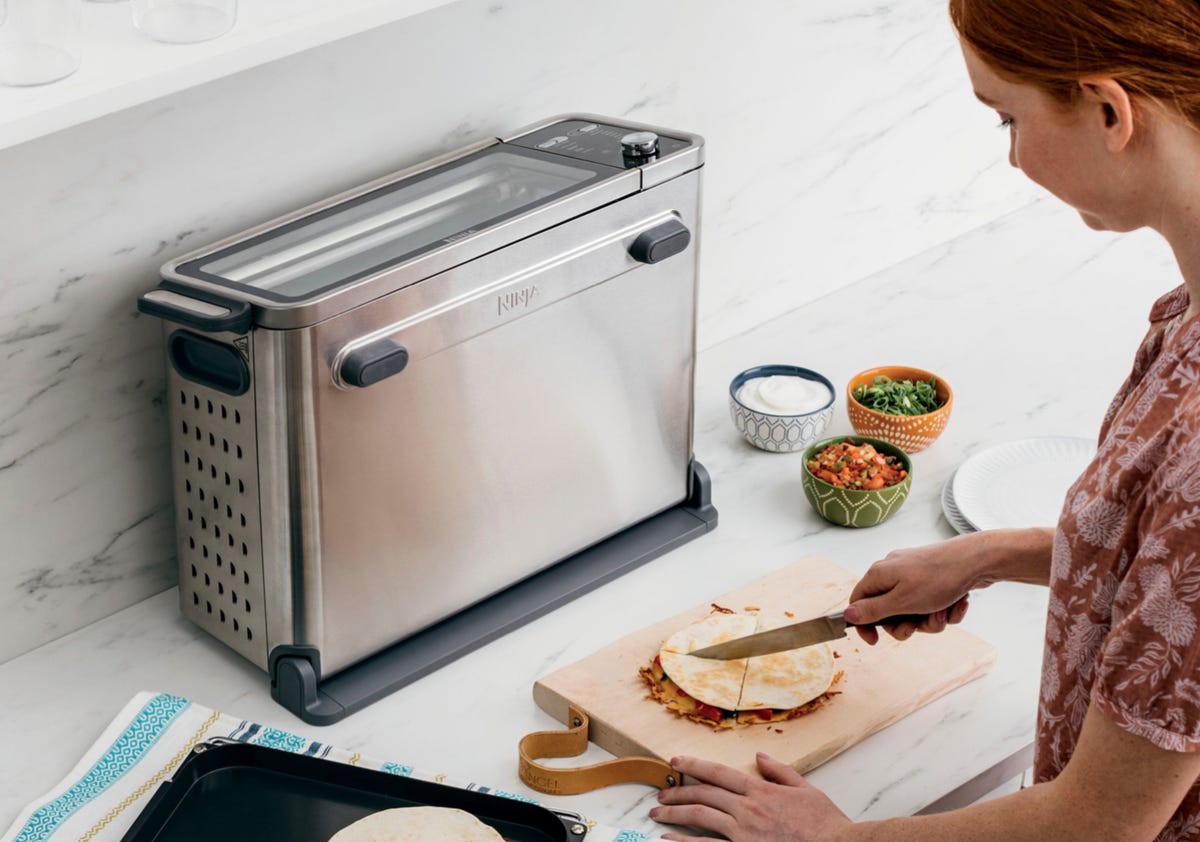 A cook cuts a fried quesadilla on the kitchen counter with the Ninja toaster-oven flipped-up to save space.