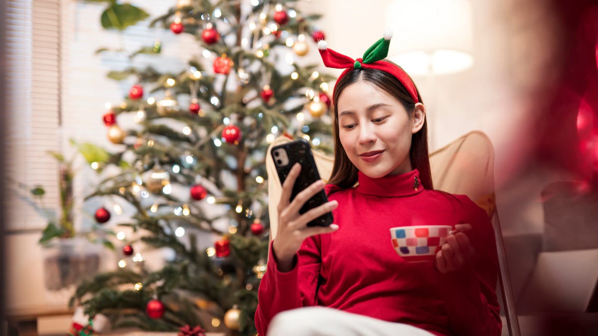 An image of a woman shopping on her phone in front of a Christmas tree.