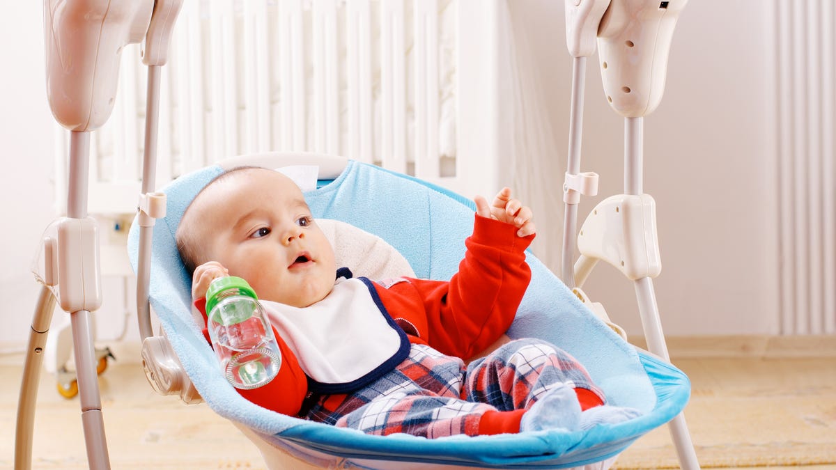Baby holding a water bottle in a baby swing, arms outstretched