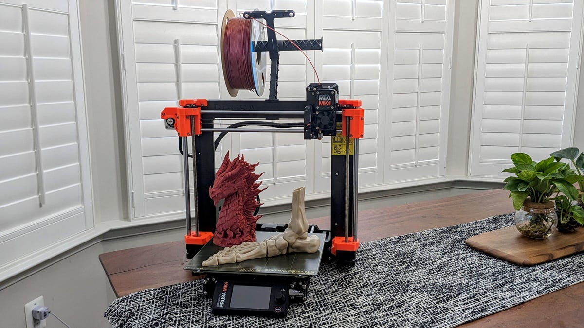 Prusa Mk4 with a dragon bust and skeleton leg on the build plate