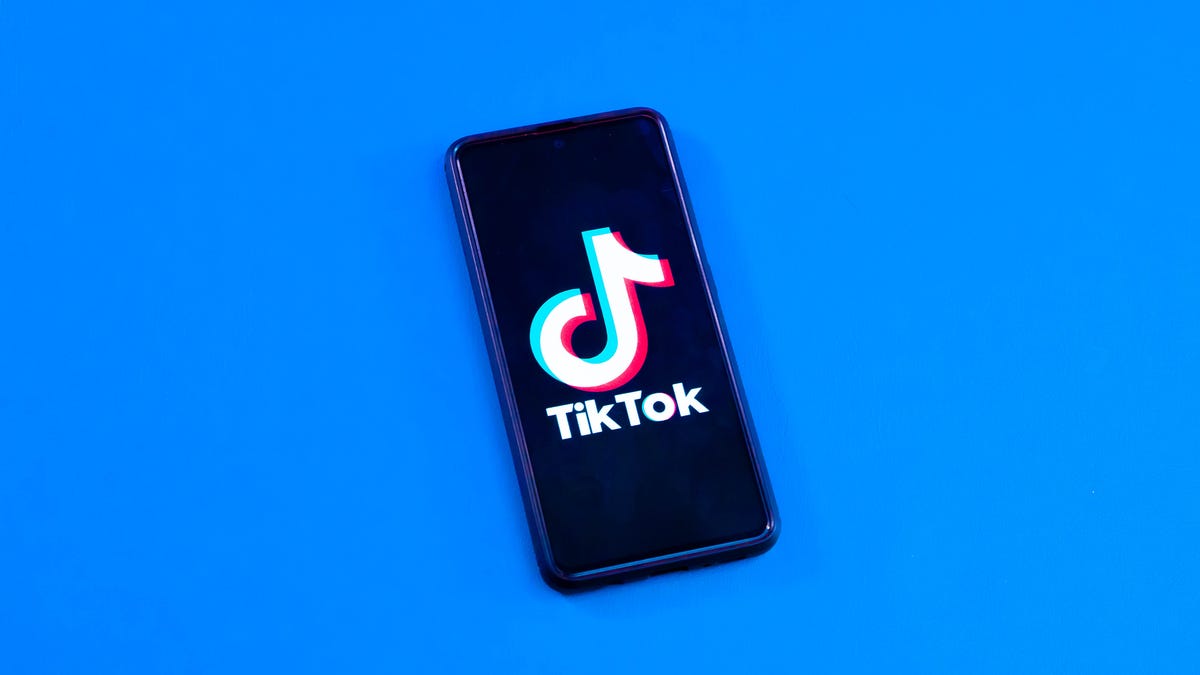TikTok's logo on a phone in front of a blue background.
