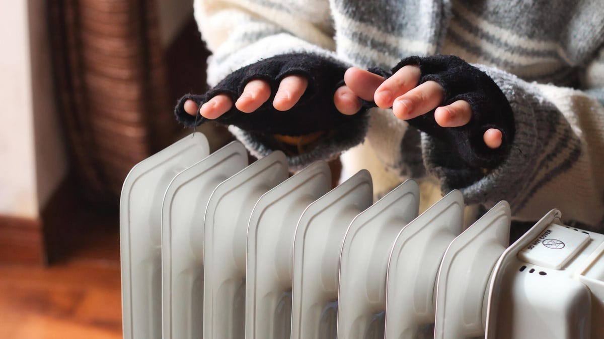 A person warms their hands over a radiator.