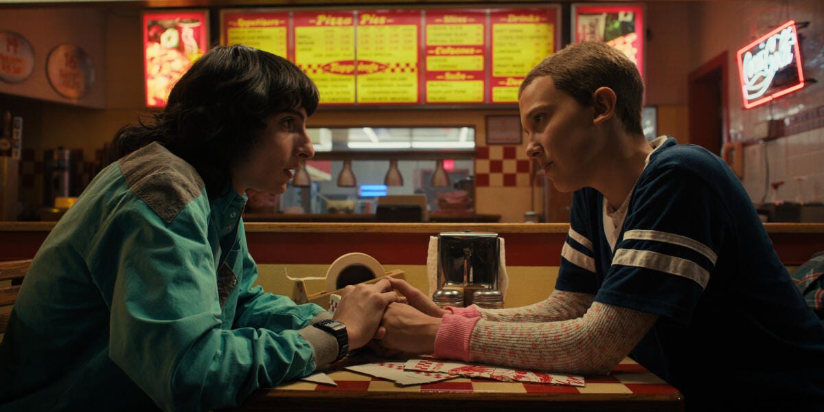 Mike and Eleven hold hands at Surfer Boy Pizza