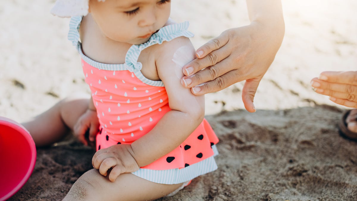 Adult putting sunscreen on a baby's arm while at the beach