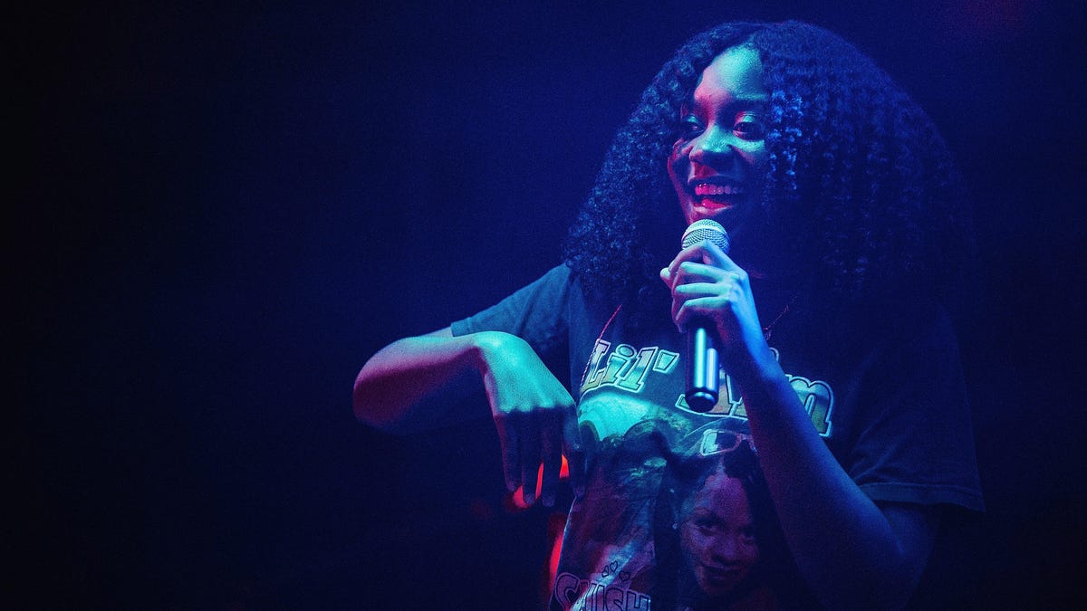 Noname stands with a mic in hand, lit by dramatic blue and red stage lighting