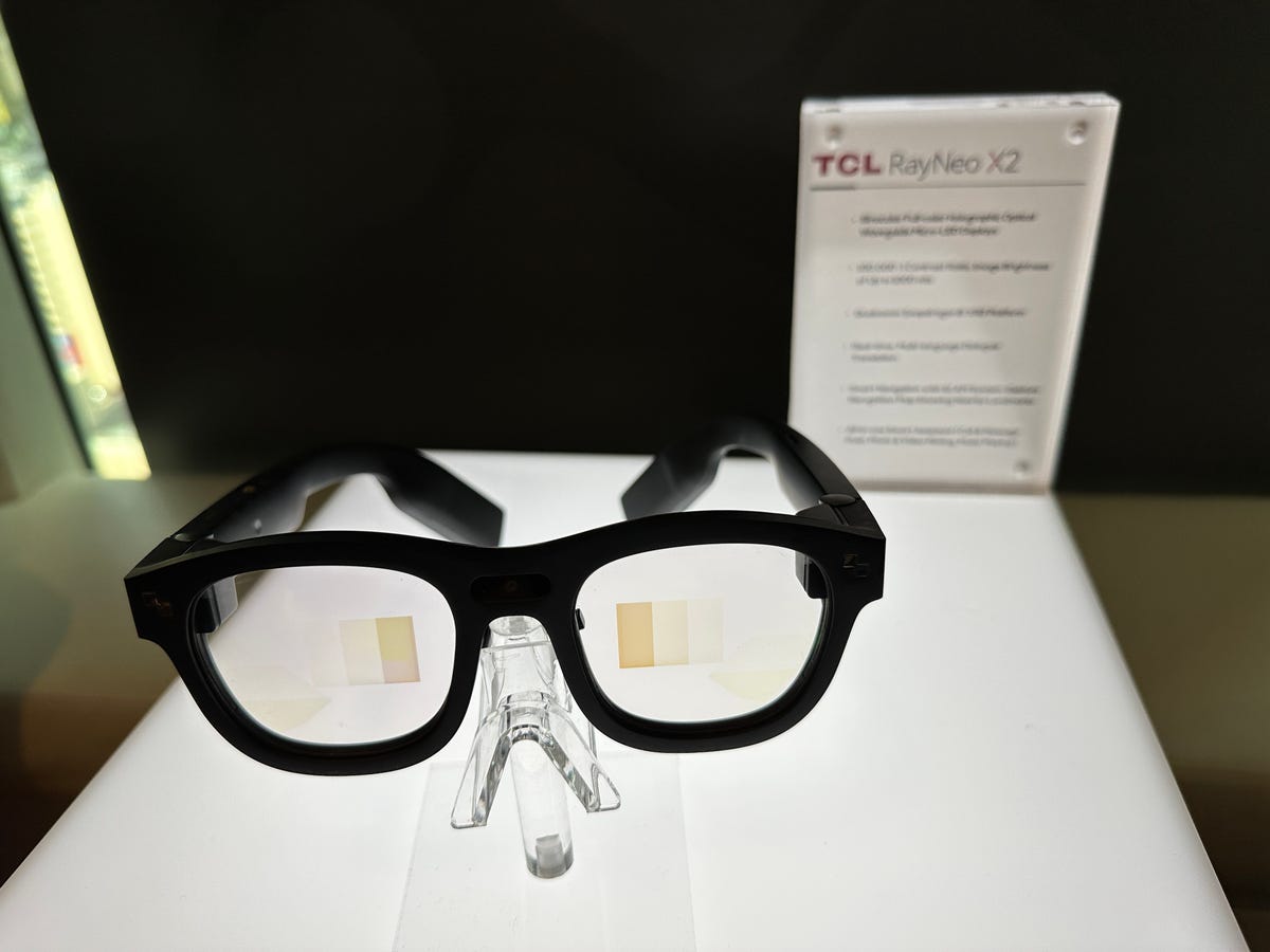 A pair of black smart glasses with clear lenses lies on a bright white table.