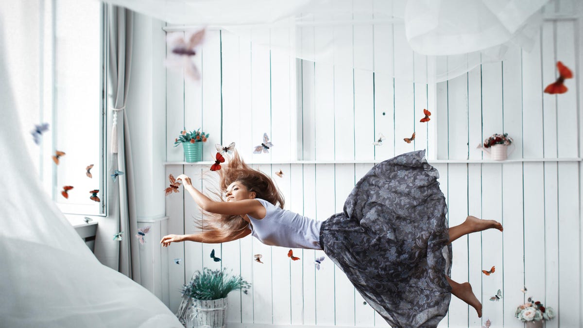 A woman floating in air in front of a window, with curtains and skirt billowing, and butterflies all around