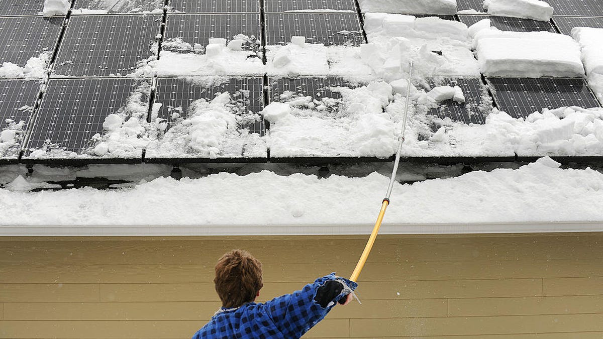 A person cleans snow off of solar panels.