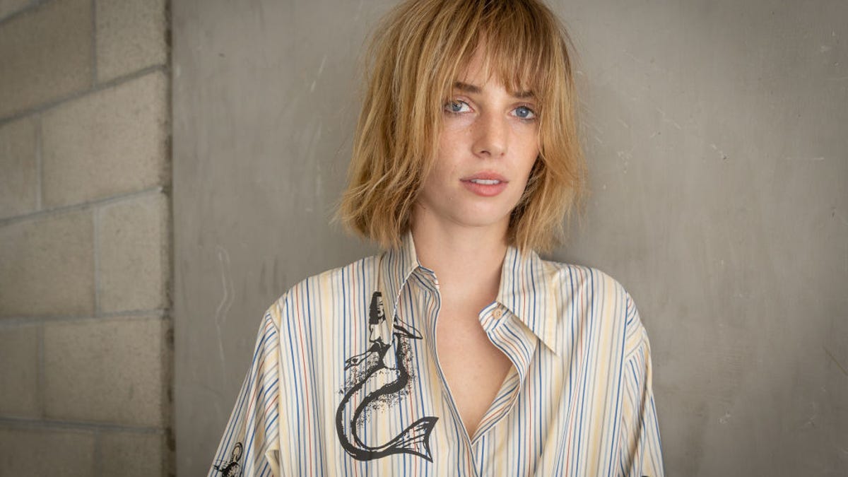 Maya Hawke looks into the camera with tousled blond hair and a button-down shirt