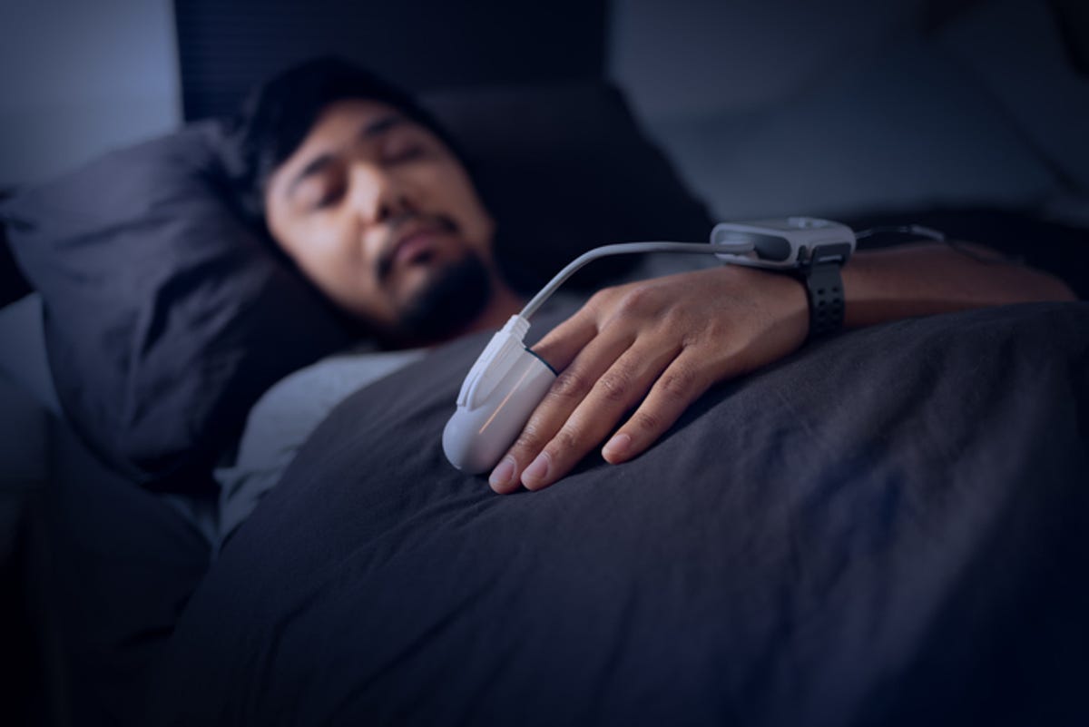 Man sleeping with a sleep apnea diagnostic device on finger and wrist.
