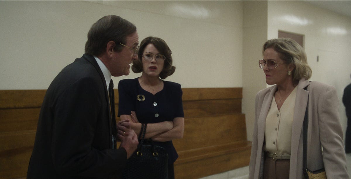 Actors Richard Jenkins, Molly Ringwald, and Penelope Ann Miller talk in a hallway in a scene from the movie Dahmer - Monster