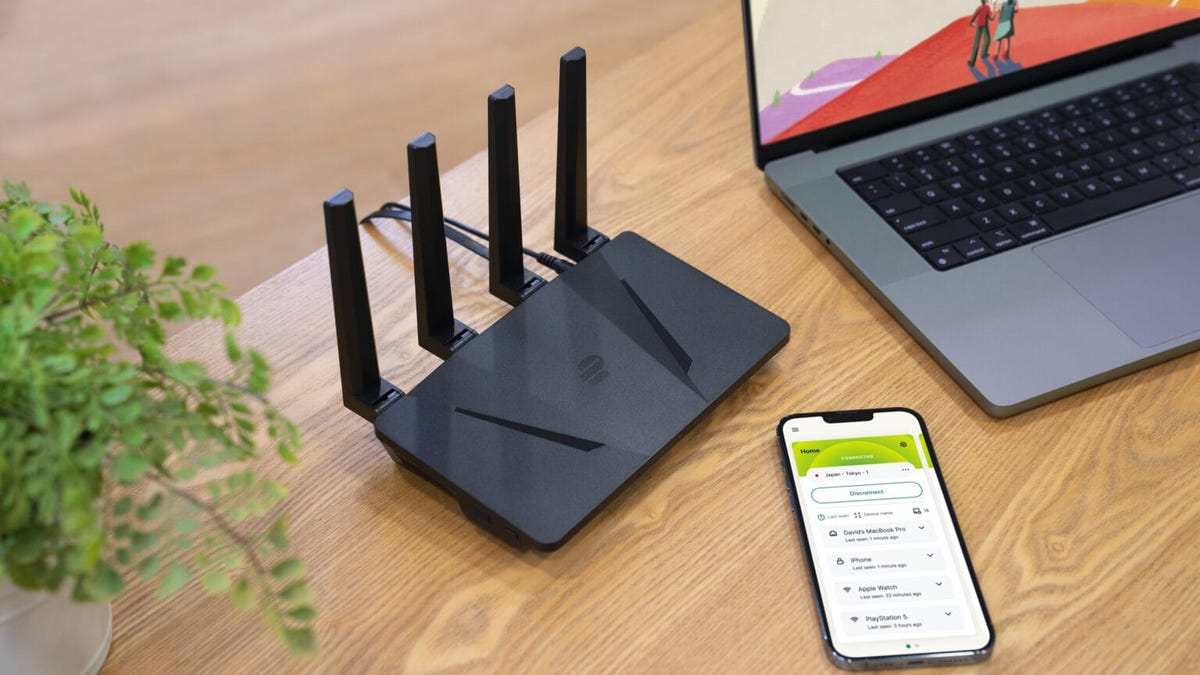 A compact router with 4 antennas rising vertically out of its back side. The router is low in profile, similar to that of a nearby cellphone and MacBook