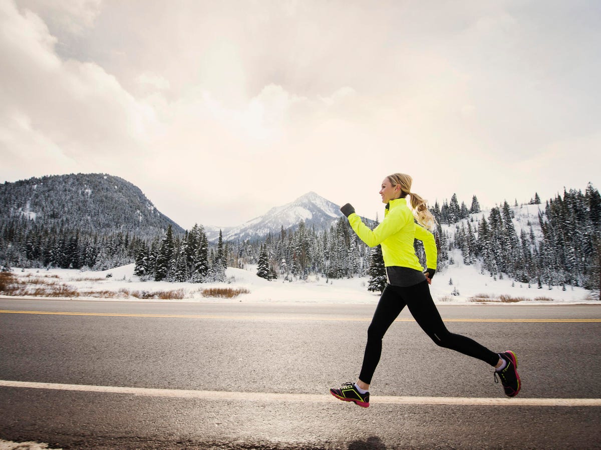 Blonde-haired woman in a neon jacket running outdoors in snowy weather.