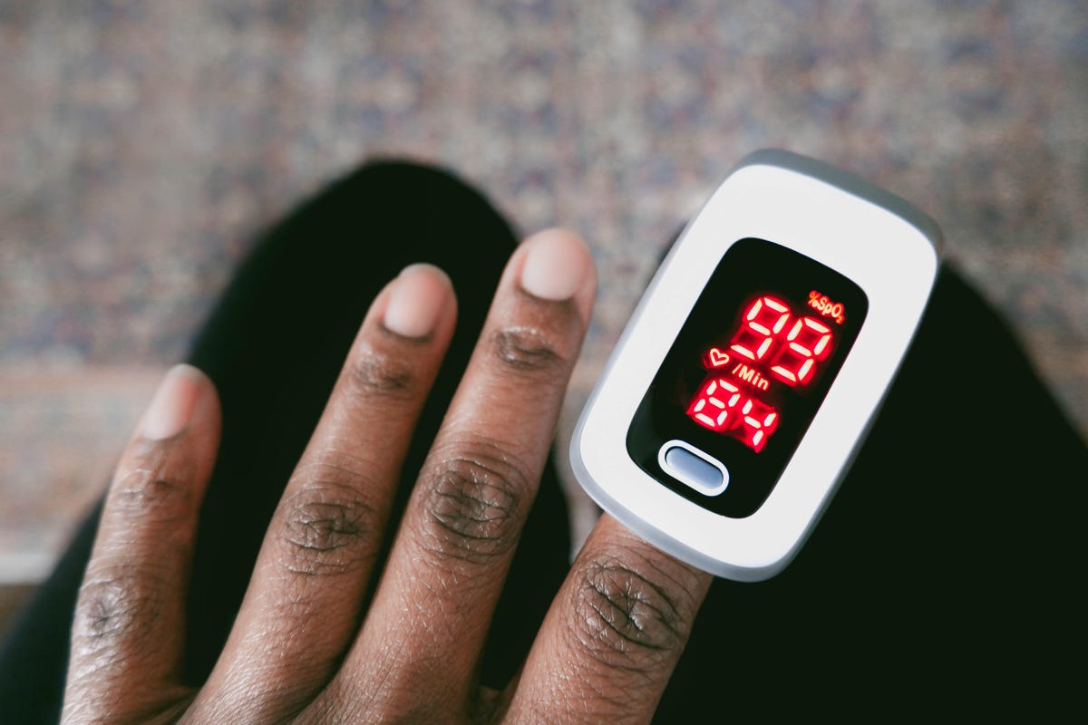 Close-up of a dark-skinned hand using a pulse oximeter.