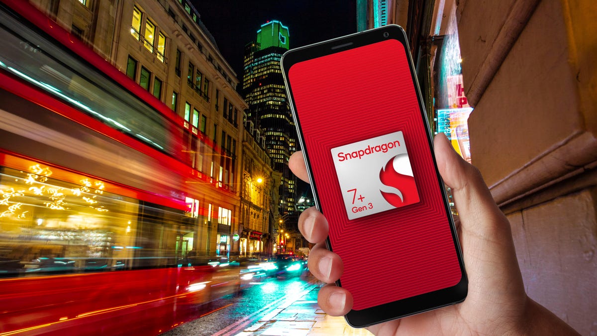 A phone with a chip logo on its screen that says "Snapdragon 7+ Gen 3", which is in front of a stylistically blurred street scene that&apos;s totally London (a red double decker bus is blurred).