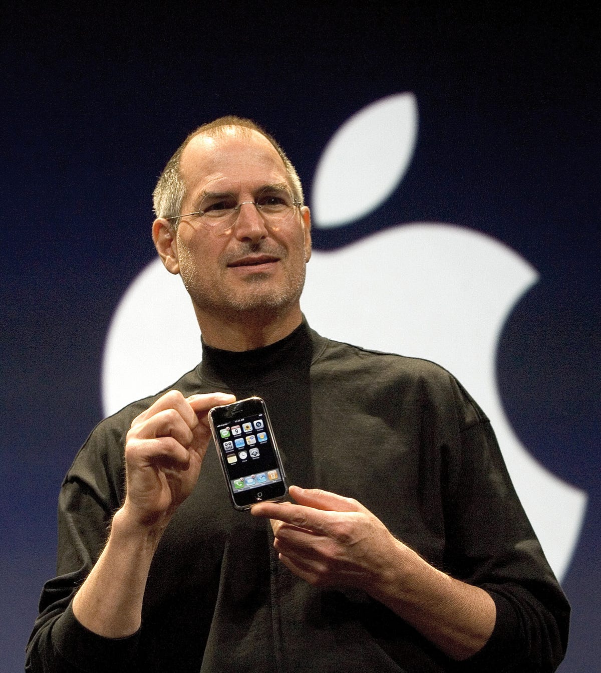 Steve Jobs in a black mock turtleneck in 2007, introducing the first iPhone, which he's holding in his hands