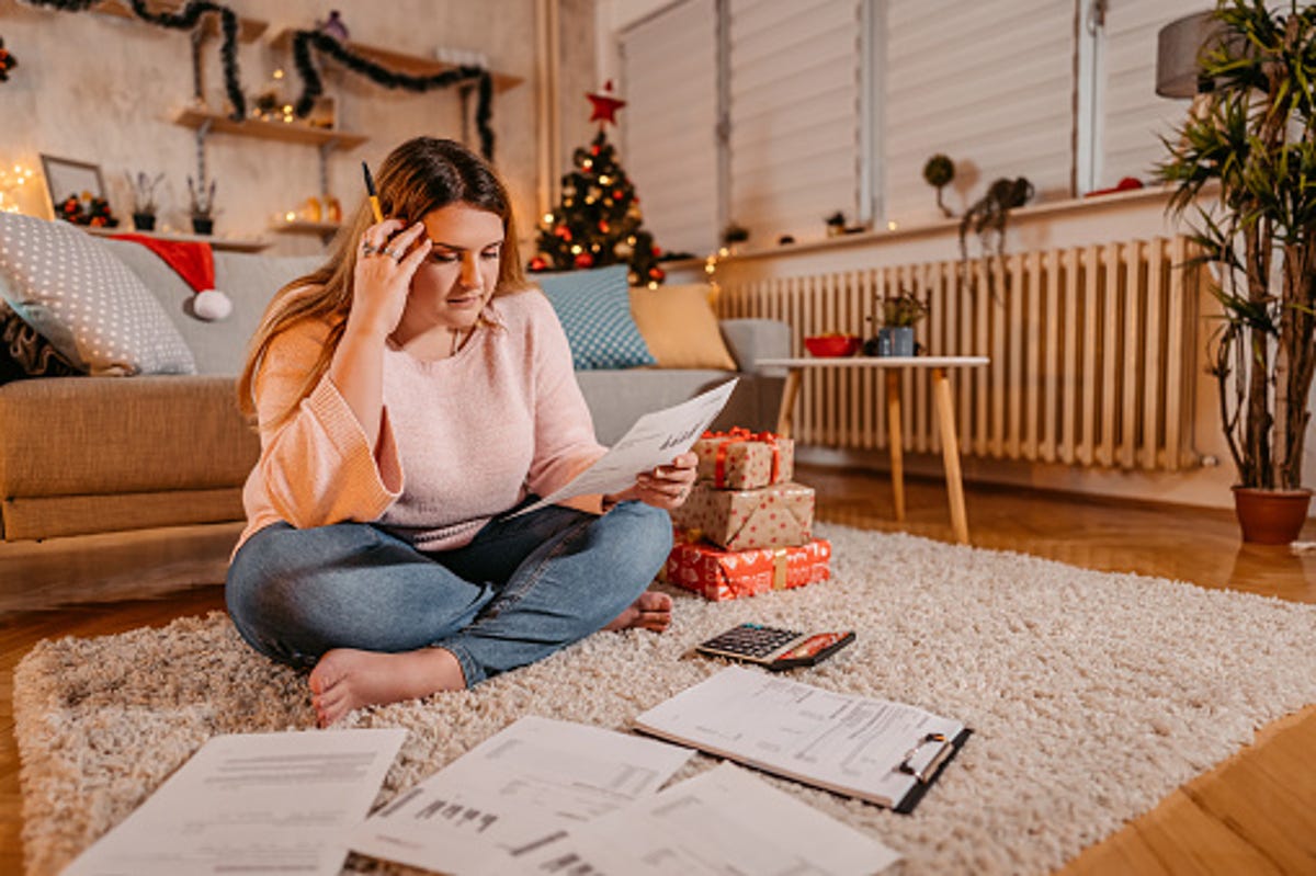 Una mujer sentada en el suelo, rodeada de papeles, planificando sus cuentas y gastos durante la temporada navideña.