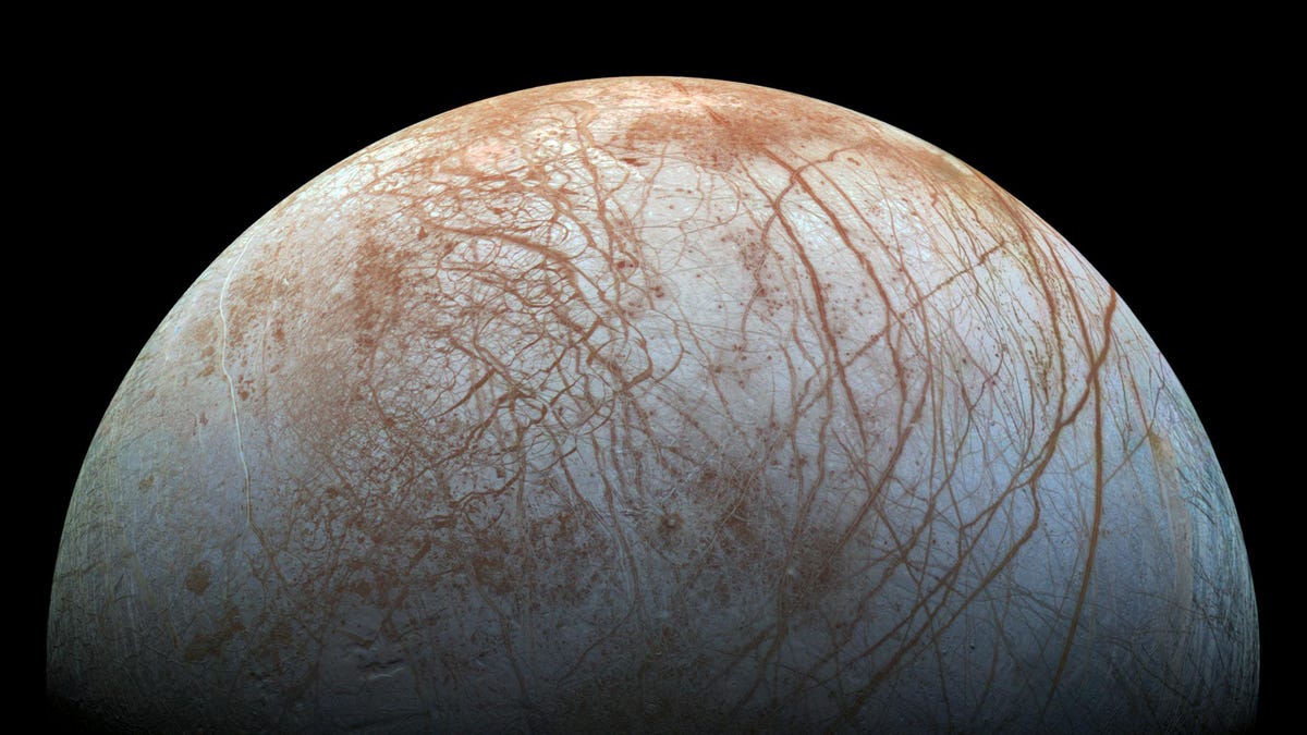 Half-moon view of Europa with reddish-brown veins over light-gray surface.
