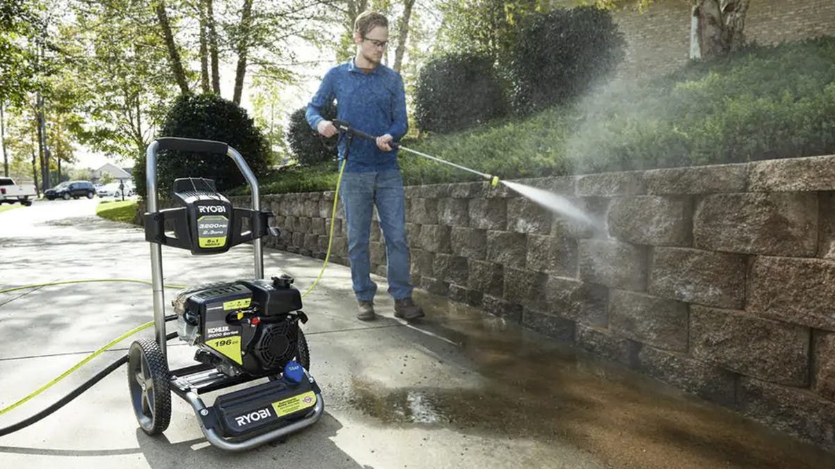 A man uses a Ryobi pressure washer to clean away stains and debris from brinks in a retaining wall.