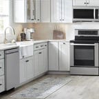 A kitchen features white and gray cabinets and a stainless steel refrigerator, dishwasher, range and microwave.