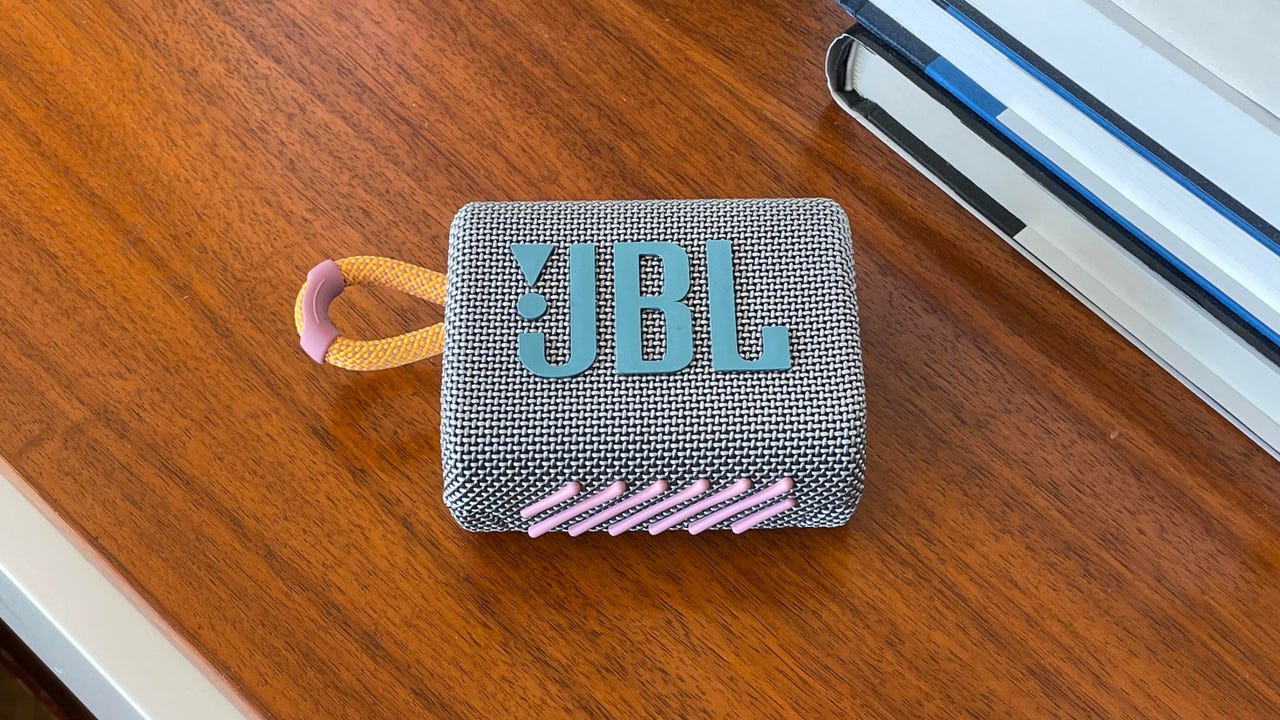 Small JBL Go 3 speaker resting on a table near a stack of books.