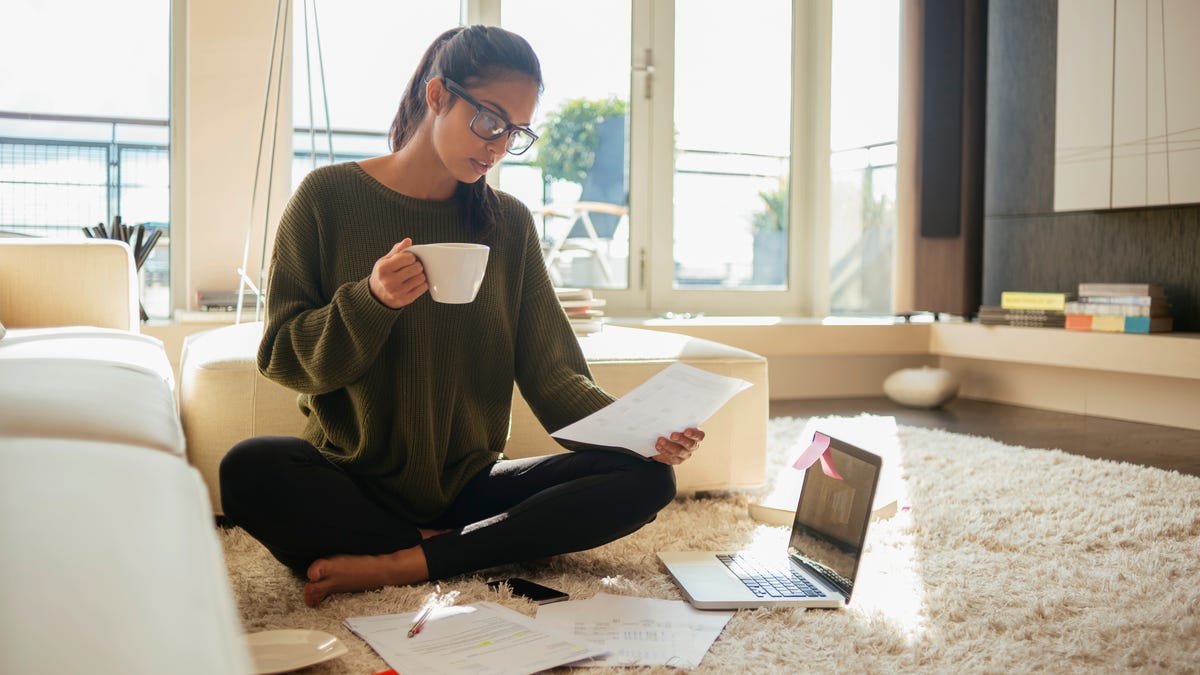A young woman sits on the floor with coffee looking at paperwork