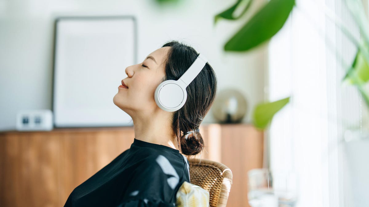 Side profile of young woman with eyes closed listening to music over headphones.
