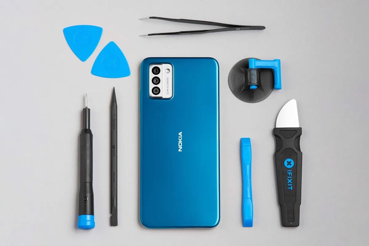 A cyan-blue Nokia G22 is surrounded by an orderly arrangement of various blue and black implements, including a large scalpel-like knife, a pair of tweezers and what look like a couple of guitar picks.