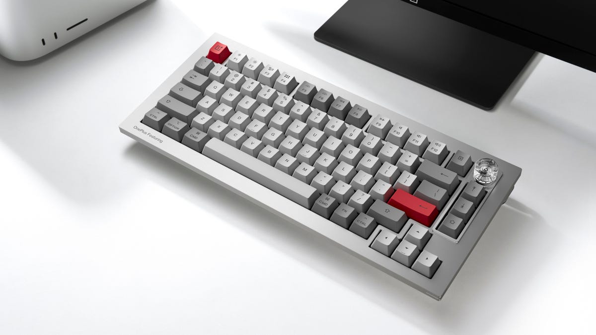The OnePlus Featuring Keyboard 81 Pro mechanical keyboard on a white desk sitting in front of a black monitor stand.