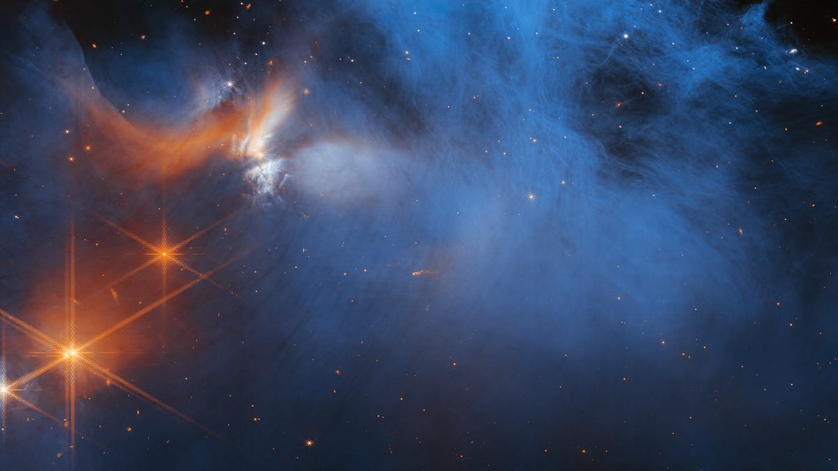 A smoky, blue-tinted view of the cosmos shows three bright stars toward the bottom left, radiating rays of light with the JWST's iconic multipointed signature.