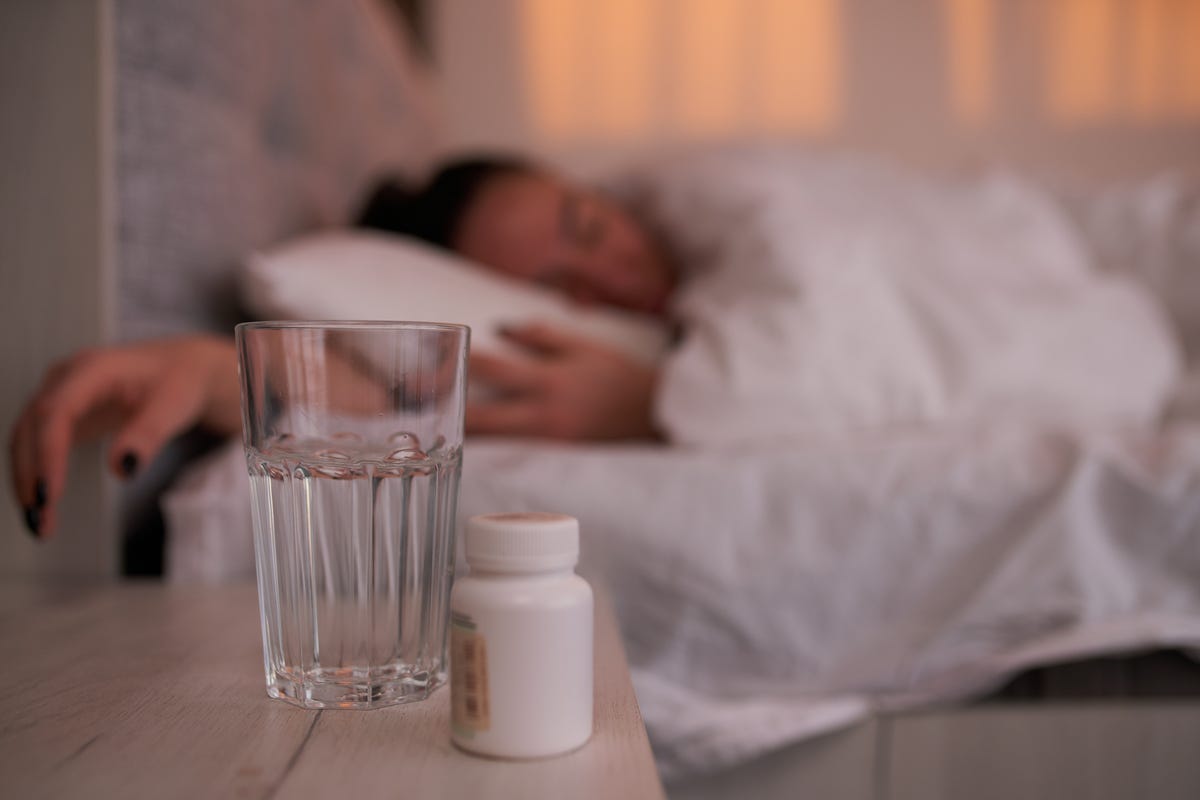 Botella de pastillas y agua en una mesita de noche.