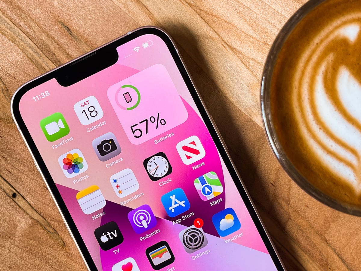 An iPhone sits on a wood table next to a coffee cup